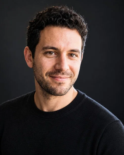 AI tech-company headshot in a black crew-neck sweater on a dark charcoal background with rim light
